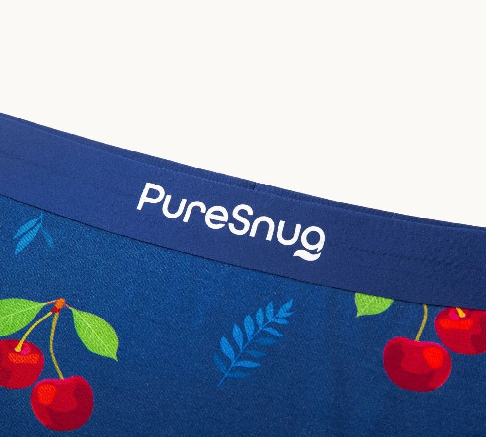 Close-up of blue underwear with a cherry and leaf pattern. The waistband features the "PureSnug" logo in white.