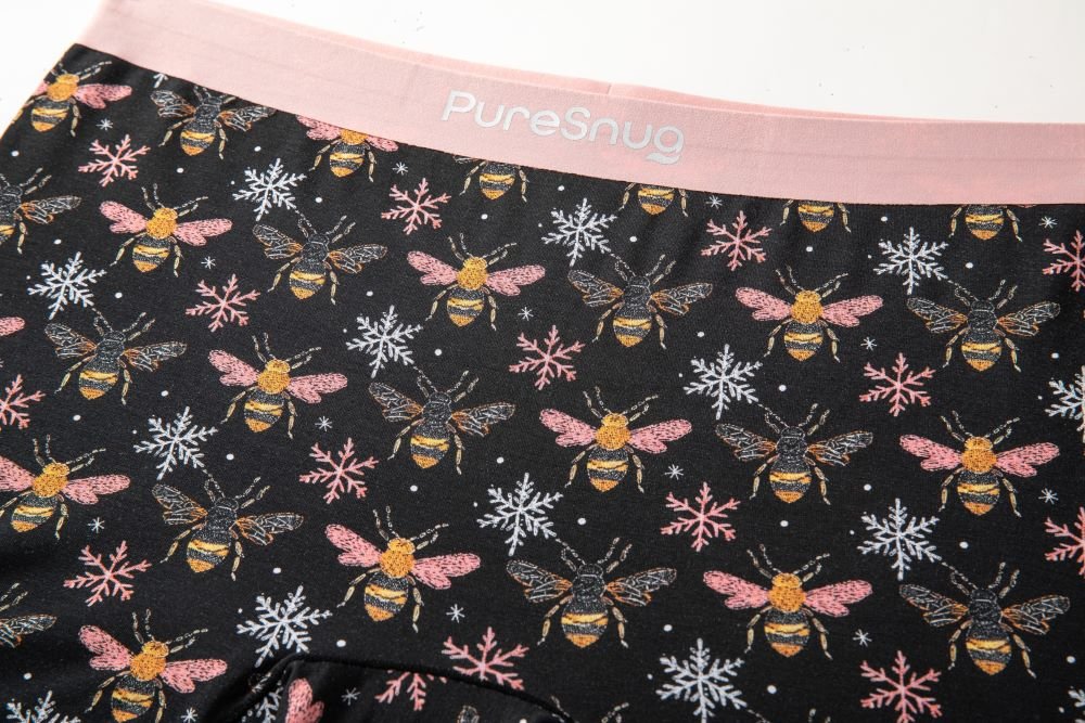 Black underwear with whimsical bee and snowflake patterns, featuring a soft pink waistband with "PureSnug" text.