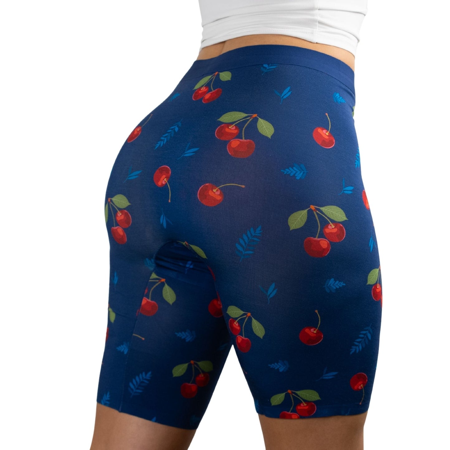 A woman in PureSnug's fitted, cherry-patterned high-waisted biker shorts with a navy background, showcasing a stylish and playful fitness look.