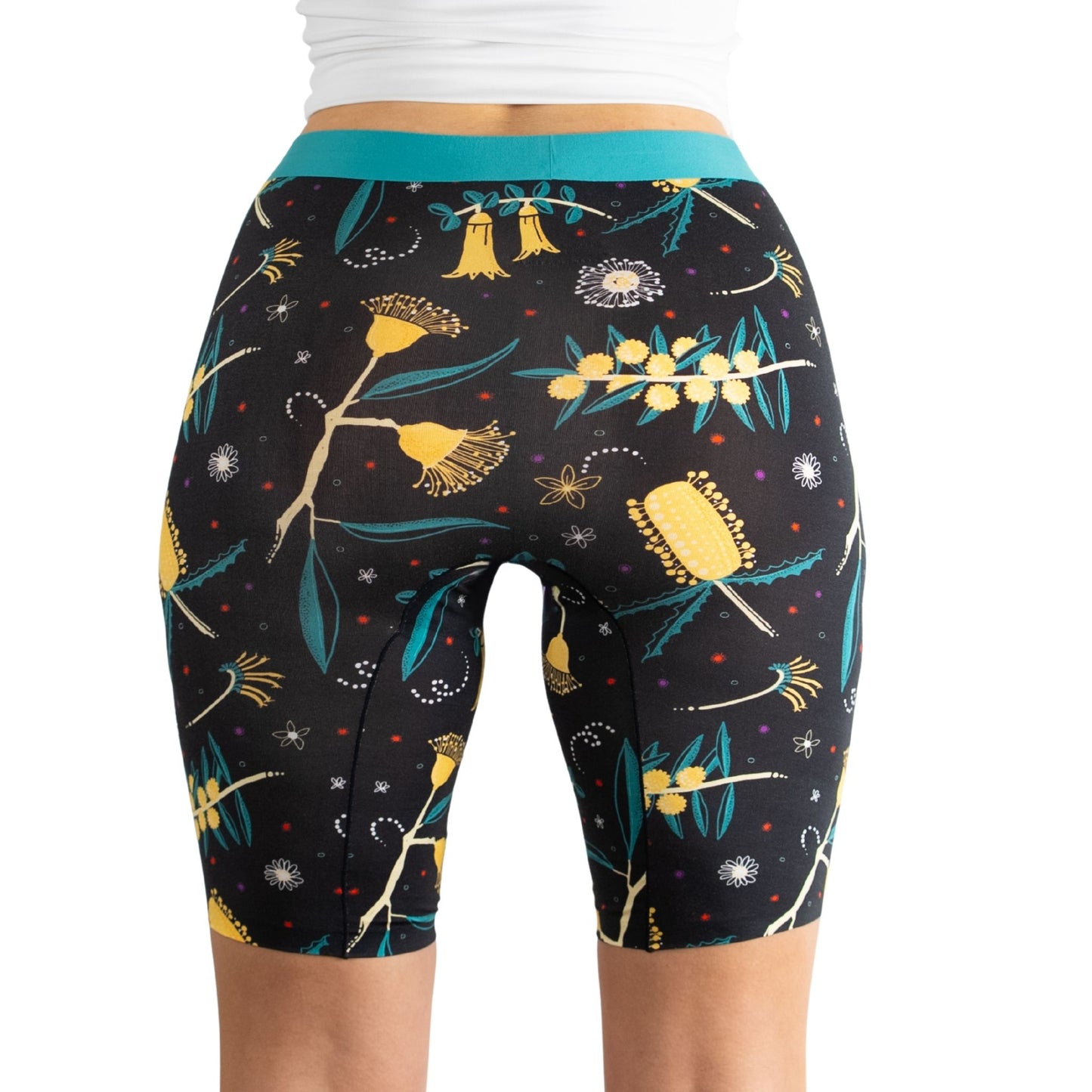 A womanβs rear view wearing floral patterned black biker shorts with a turquoise waistband and white crop top.