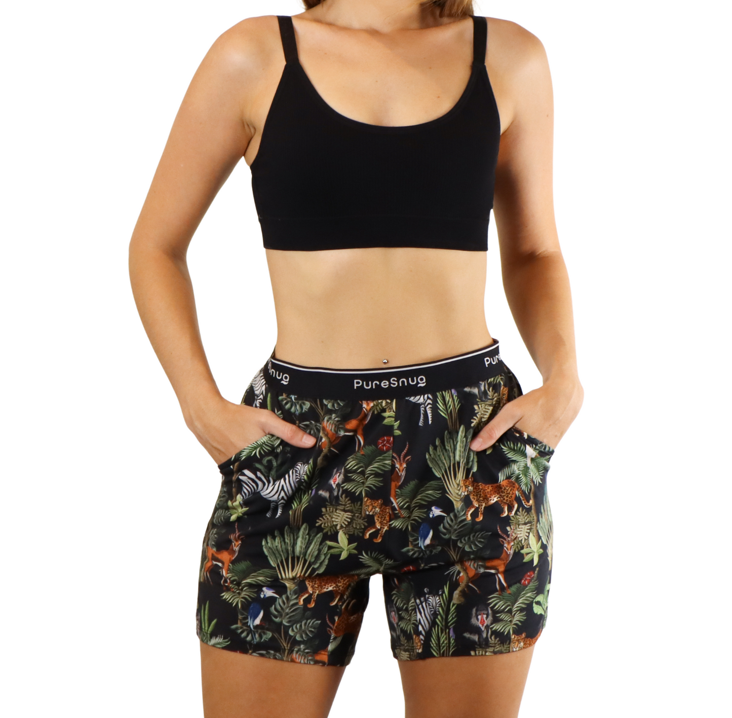 A woman in a black sports bra and tropical patterned shorts stands with hands in pockets, showcasing a vibrant, nature-inspired design.