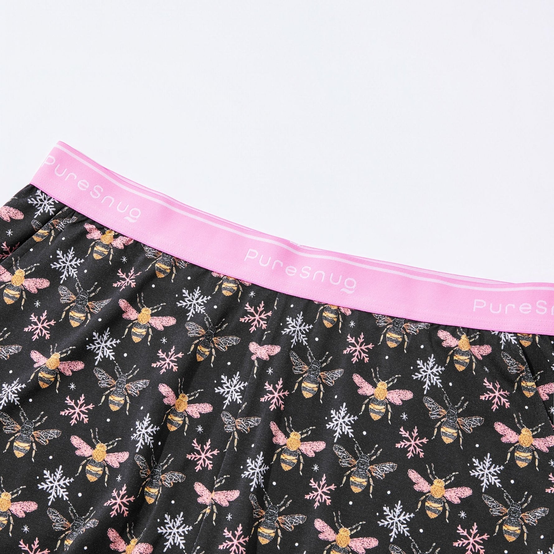 Black lounge shorts with bee and snowflake pattern and pink waistband, featuring 'PureSnug' branding.