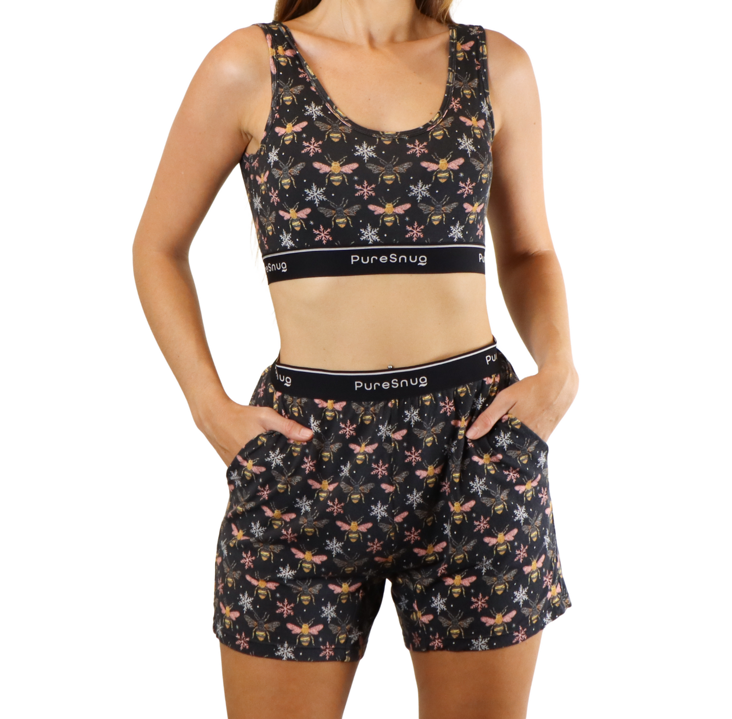 A woman models a black floral sports bra and matching shorts, both featuring a bee and flower pattern, with comfortable pockets.