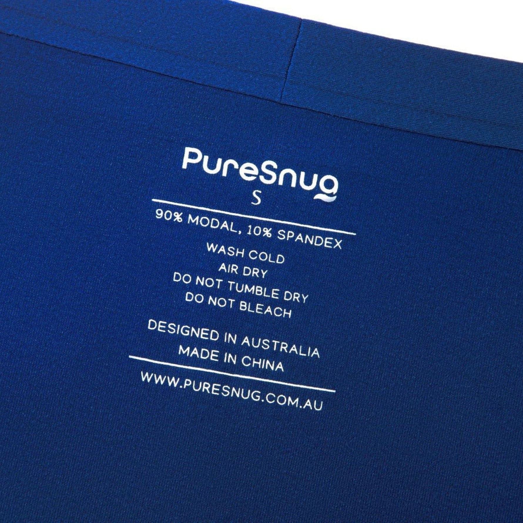 Close-up of a garment care label on blue fabric. It reads "PureSnug S, 90% Modal, 10% Spandex," with washing instructions.