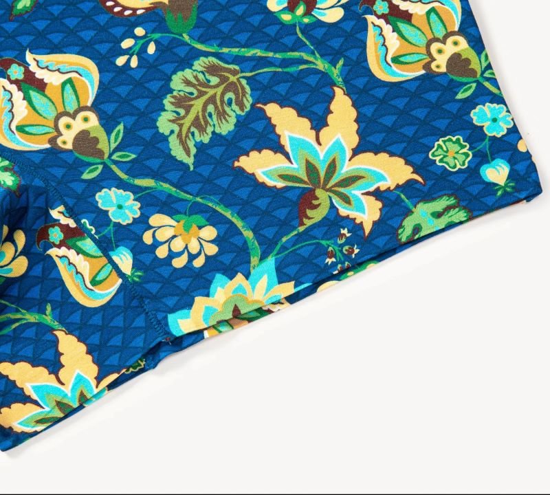 Close-up of vibrant fabric with a floral pattern on a blue background. Features green, yellow, and orange leaves and flowers