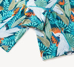 Fabric with vibrant tropical print featuring white cockatoos, orange crests, teal and green leaves.