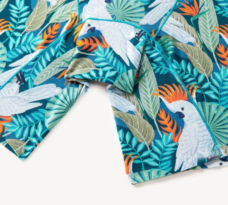 Fabric with vibrant tropical print featuring white cockatoos, orange crests, teal and green leaves.