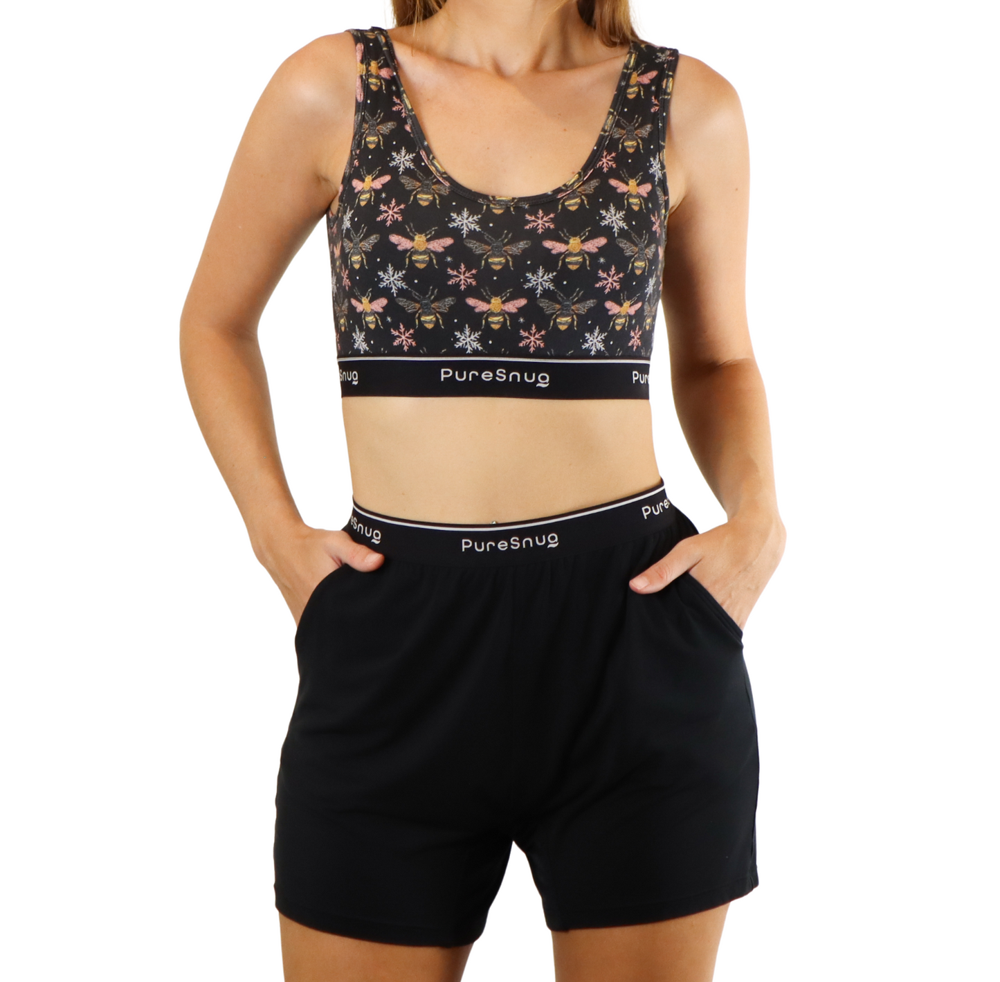 A woman models a bees-print crop top with a Puresnug logo, paired with black shorts featuring a comfortable waistband.