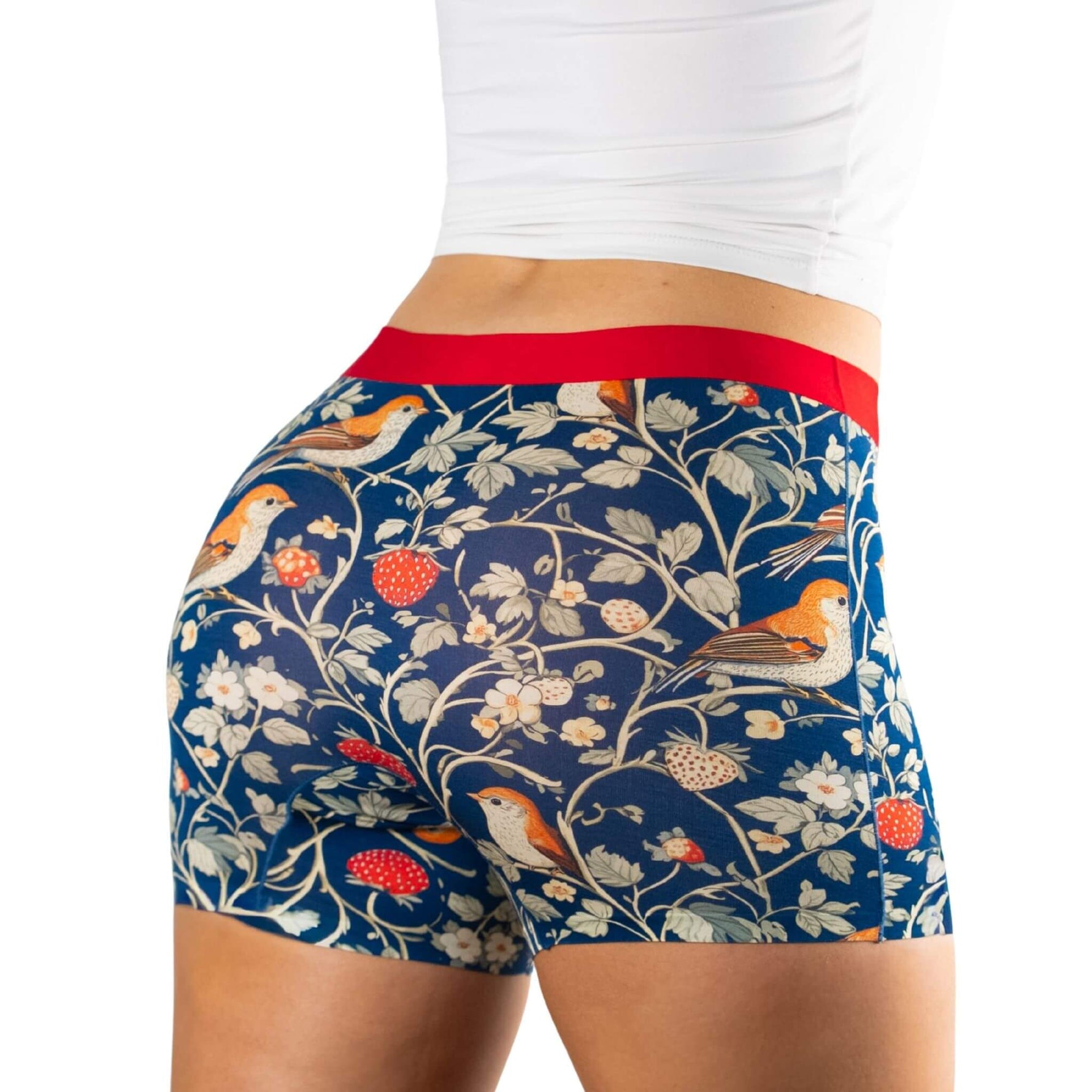 A close-up of a person wearing colorful patterned shorts featuring berries, birds and flowers, with a contrasting red waistband.