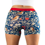 A close-up of blue patterned boxer shorts featuring birds and strawberries, with a red waistband, worn by a model.