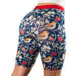 A close-up of a woman's backside wearing patterned shorts featuring birds and strawberries against a dark blue background.