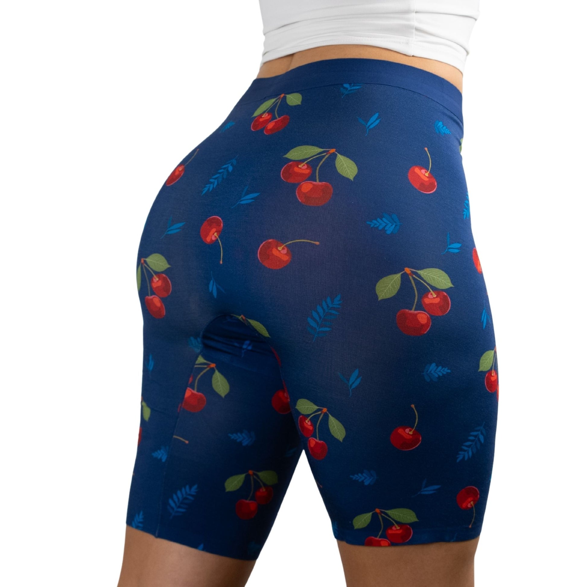 A woman in PureSnug's fitted, cherry-patterned high-waisted biker shorts with a navy background, showcasing a stylish and playful fitness look.