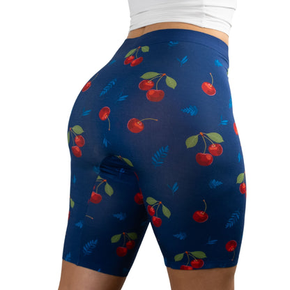 A woman in PureSnug's fitted, cherry-patterned high-waisted biker shorts with a navy background, showcasing a stylish and playful fitness look.