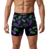 A man wearing colorful boxer shorts featuring purple eggplant and green leaves on a black background.