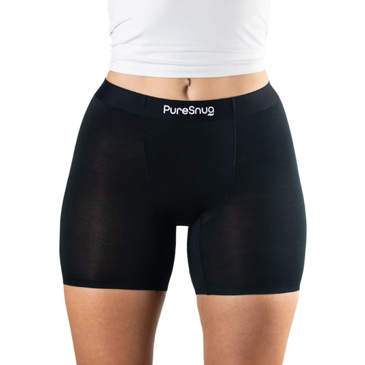 A close-up of a woman's waist and thighs wearing black PureSnug leak proof undies, paired with a fitted white top.