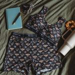 A lounge wear set featuring a crop top bra and lounge shorts lies on an olive green bedspread, accompanied by a notebook, pen, and water bottle.
