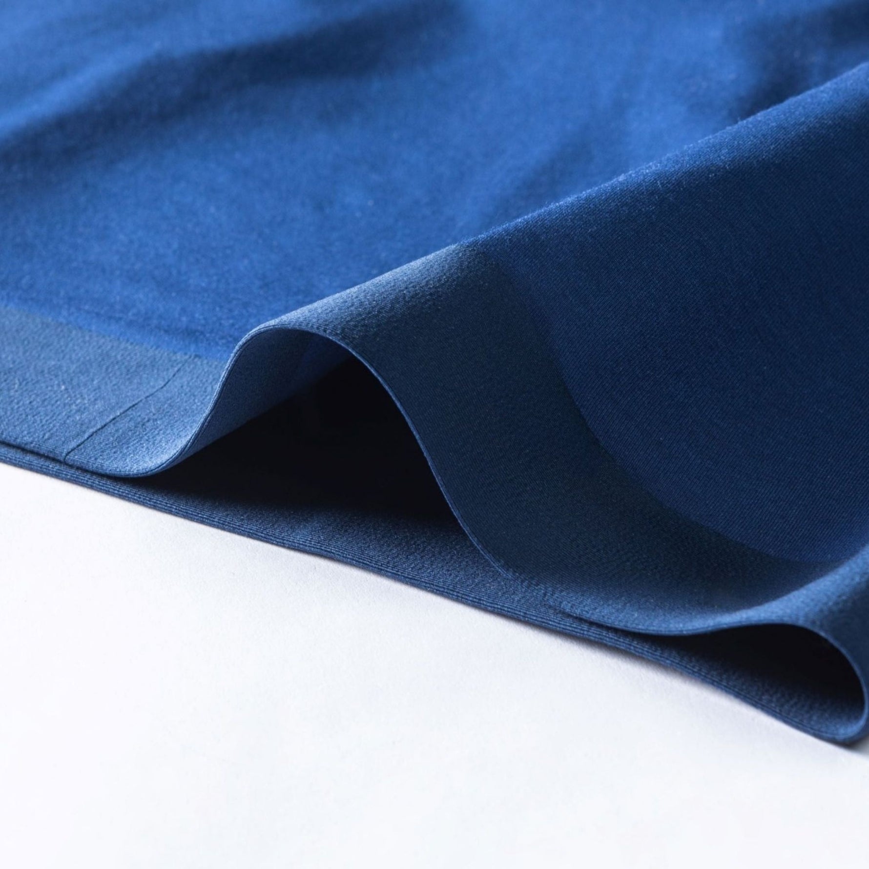 Close-up of soft, navy blue fabric with elegant draping and gentle folds, highlighting its smooth texture against a light