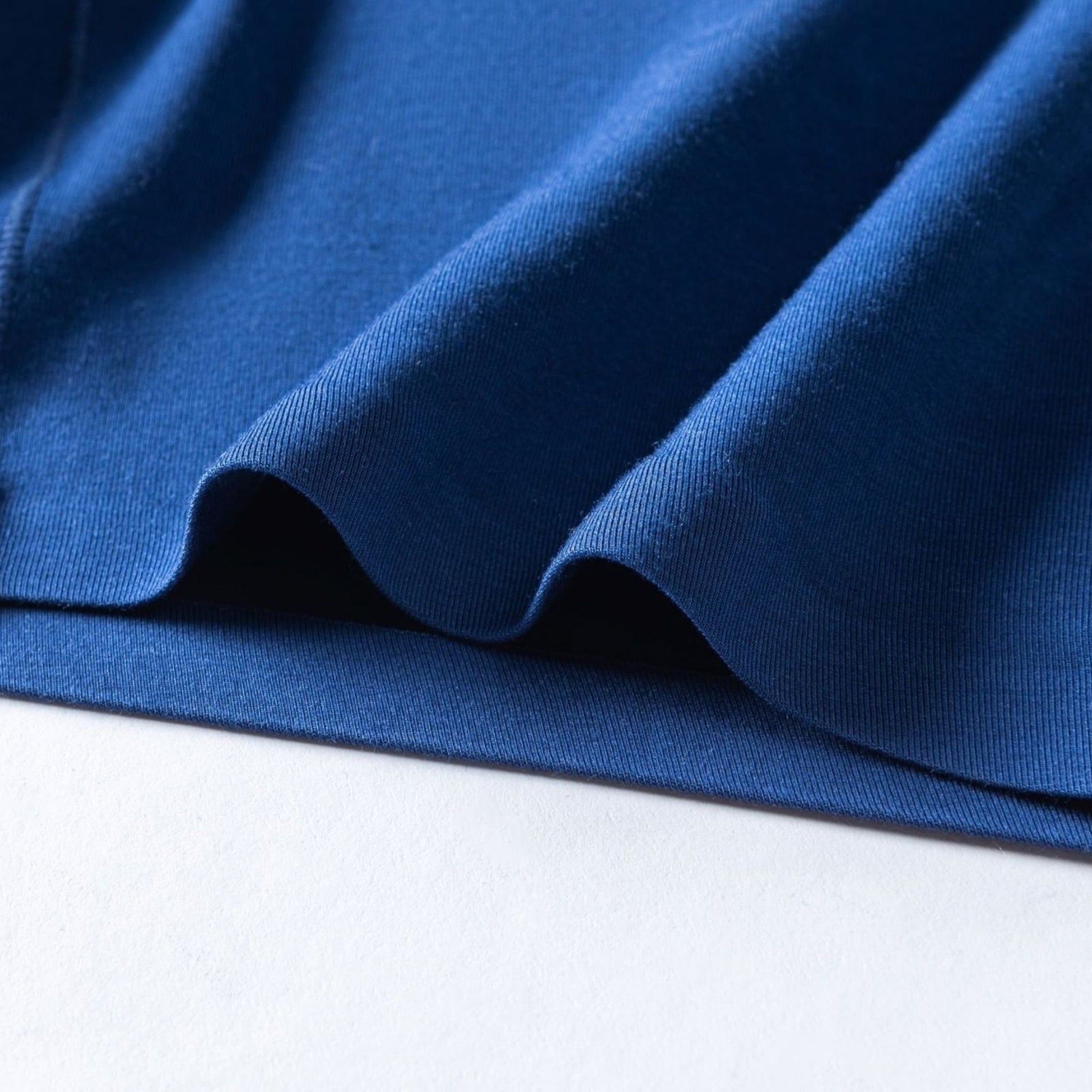 Close-up of gently folded blue fabric, showcasing its smooth texture and subtle sheen against a crisp white background.