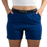Close-up of a person wearing PureSnug's Navy blue lounge shorts with "PureSnug" on the waistband. Hands in pockets. 
