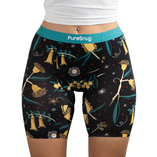 A close-up of a person wearing PureSnug Golden Snug boxer brief in floral-patterned black shorts with a turquoise waistband, featuring vibrant botanical prints.