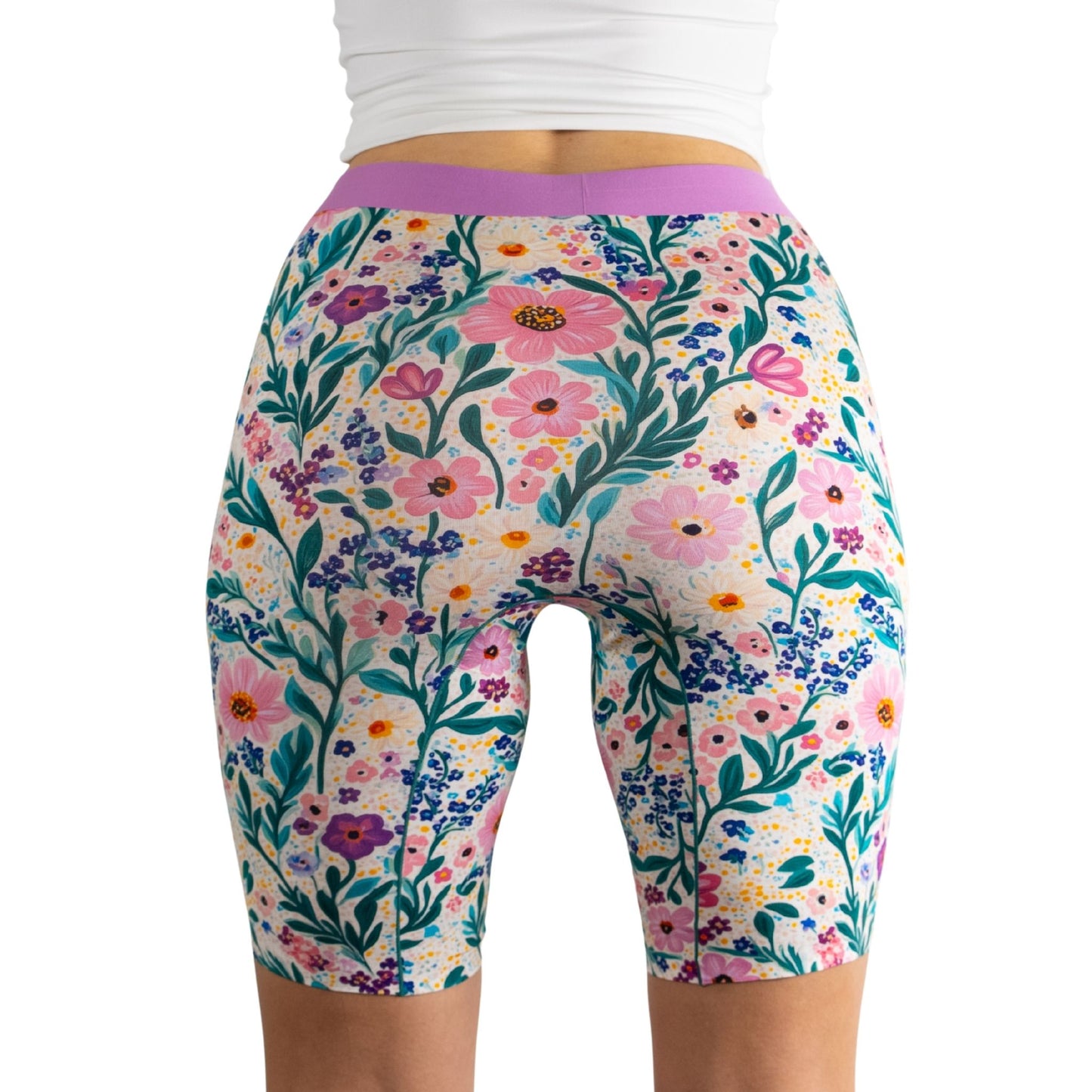 A model in a white top showcases colorful, floral-patterned bike shorts, highlighting vibrant blooms and greenery.