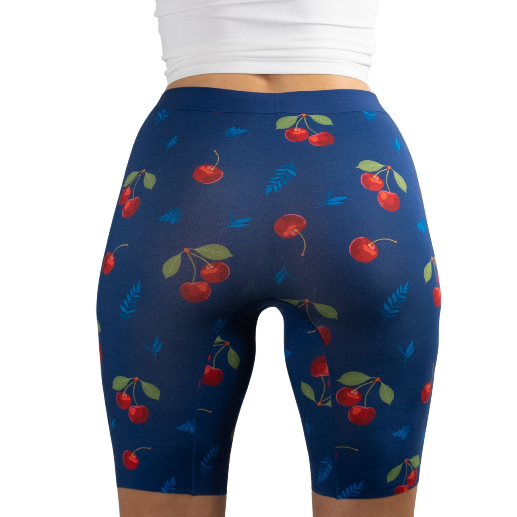 A woman in a white top wears PureSnug's high-waisted 8" biker shorts with a vibrant cherry pattern. The design is playful and colorful, conveying a fun, summery vibe.