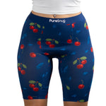 A close-up of a person wearing navy shorts adorned with vibrant cherry and leaf patterns, featuring the PureSnug brand logo.