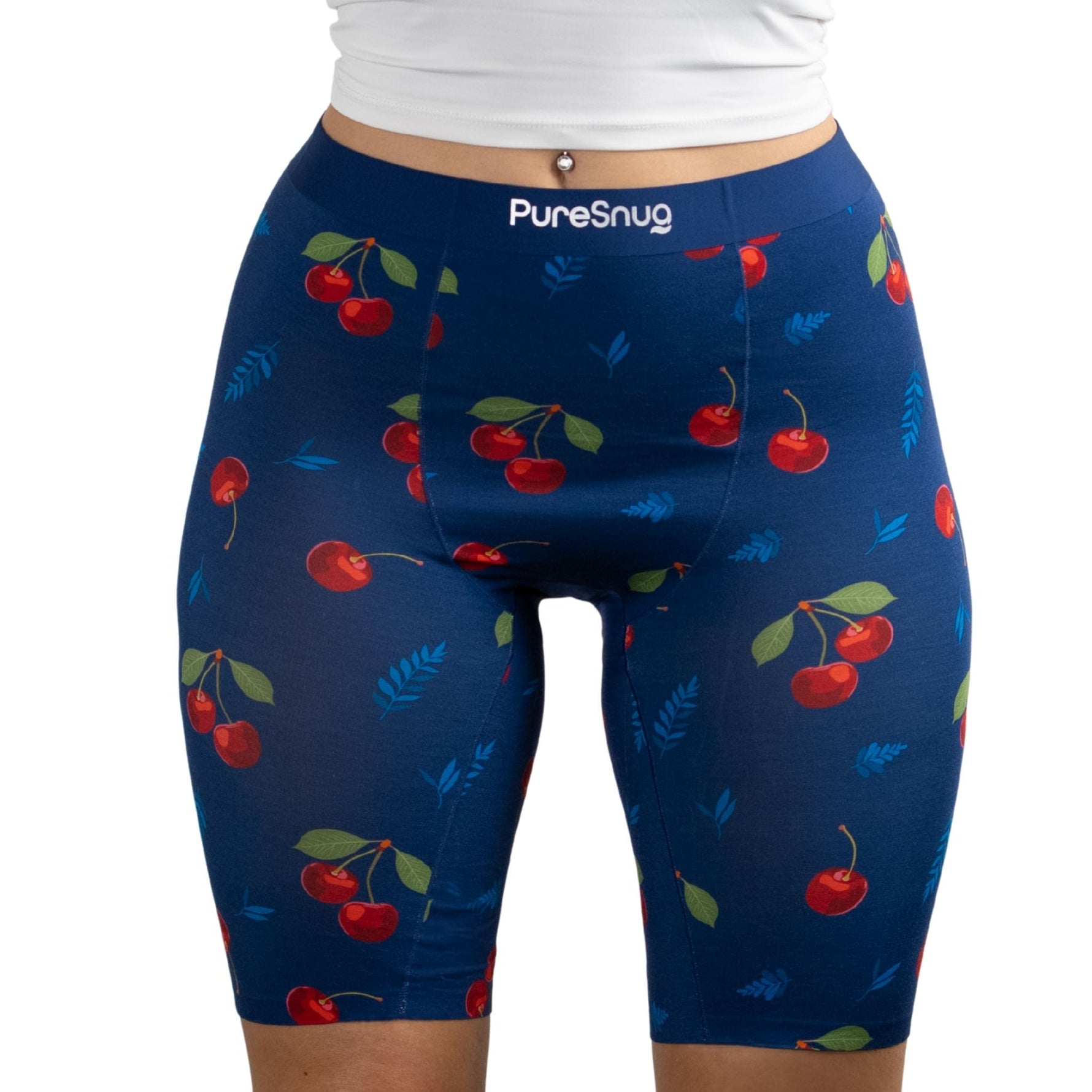 A close-up of a person wearing navy shorts adorned with vibrant cherry and leaf patterns, featuring the PureSnug brand logo.