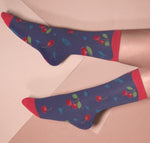 Two legs in blue socks with red cherry patterns, cuffs, and toes, set against a muted pink background for a playful look.