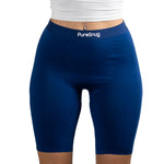 A model wearing navy blue PureSnug high-waisted bike shorts, paired with a white cropped top