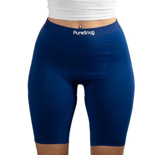 A model wearing navy blue PureSnug high-waisted bike shorts, paired with a white cropped top, showcasing a casual athletic look.