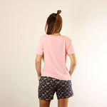 A woman wears a soft v-neck Tee in pink colour, and a soft lounge shorts in bees prints, with hands in pockets, back view.