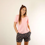 A woman wears a soft v-neck Tee in pink colour, and a soft lounge shorts in bees prints, with hands in pockets.