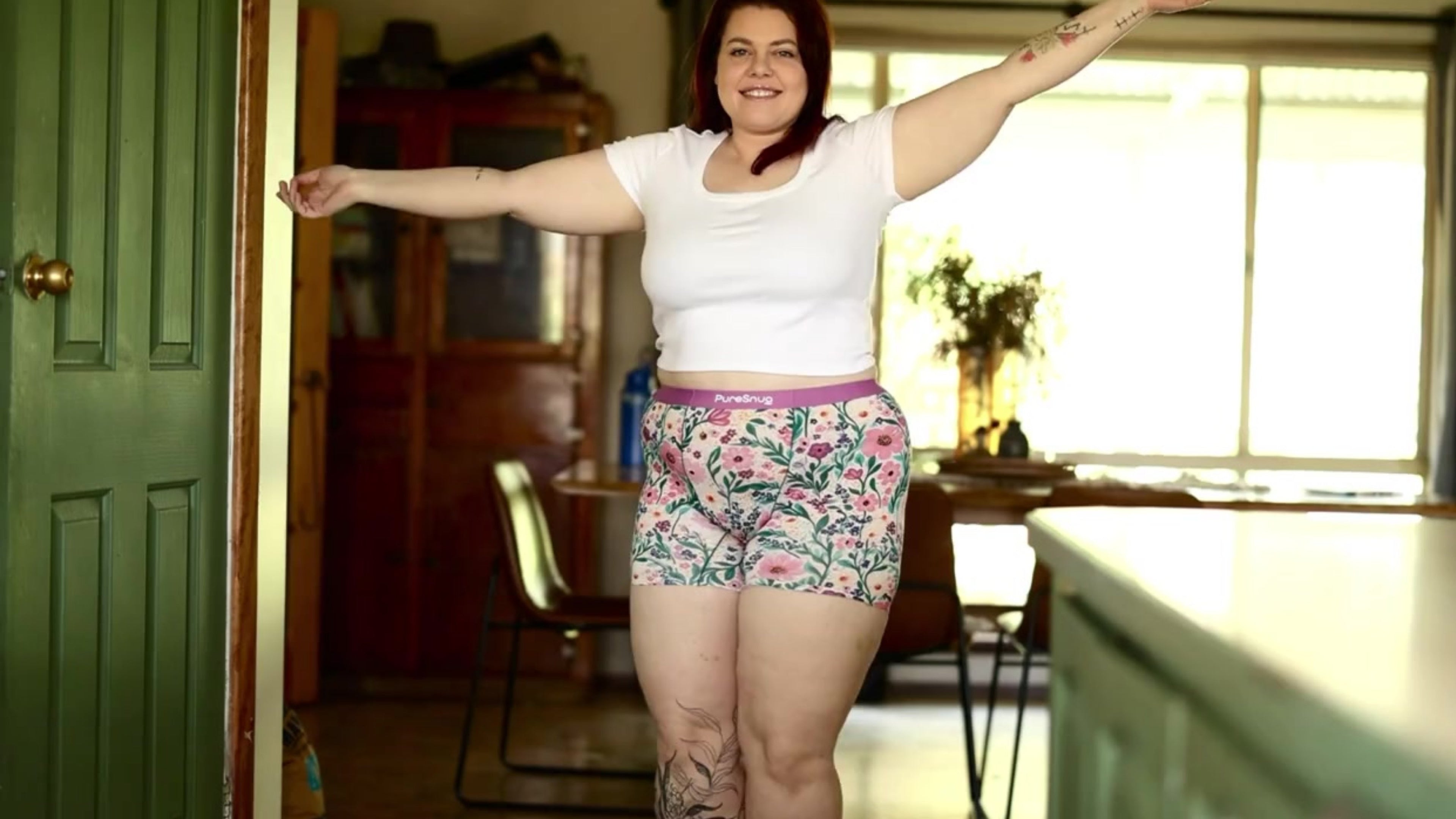 Load video: A confident woman dancing in a  living room, wearing a white crop top and floral PureSnug boxer briefs — showcasing size-inclusive, no-ride-up underwear designed for comfort and joyful movement.
